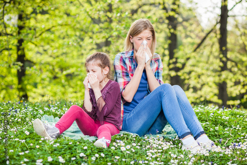 Two people with allergy symptom blow their noses photo