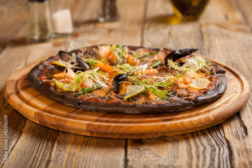 Italian pizza "Di Mare" with black dough and seafood on wooden t