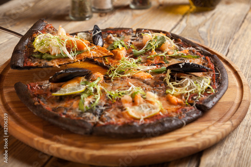 Italian pizza "Di Mare" with black dough and seafood on wooden t