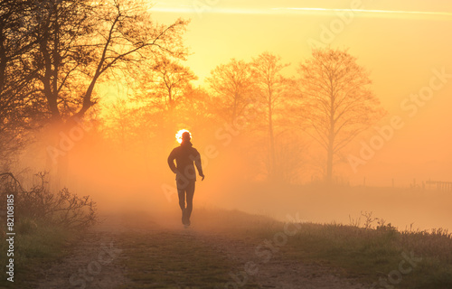 Runner on a gravel road during a foggy, spring sunrise.