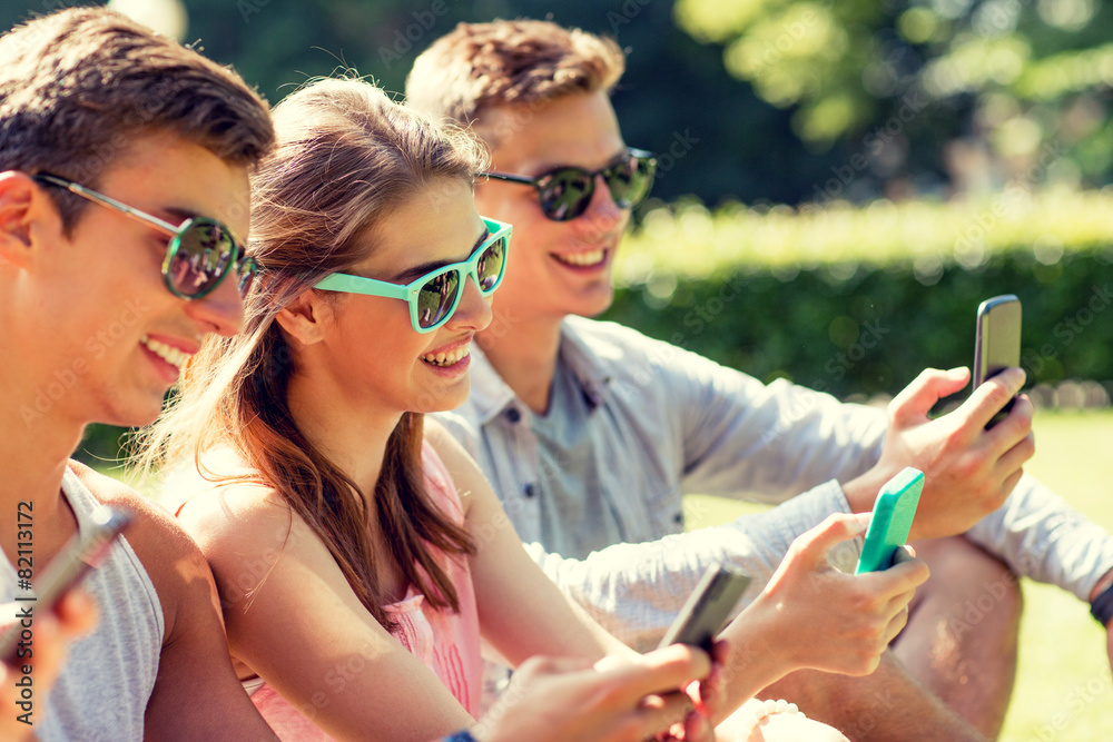 smiling friends with smartphones sitting on grass smiling friends with smartphones sitting on grass