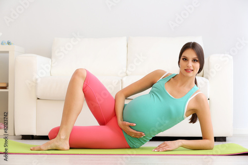 Pregnant woman exercising on green mat in room