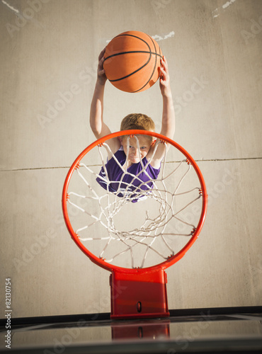 Caucasian boy dunking basketball in hoop