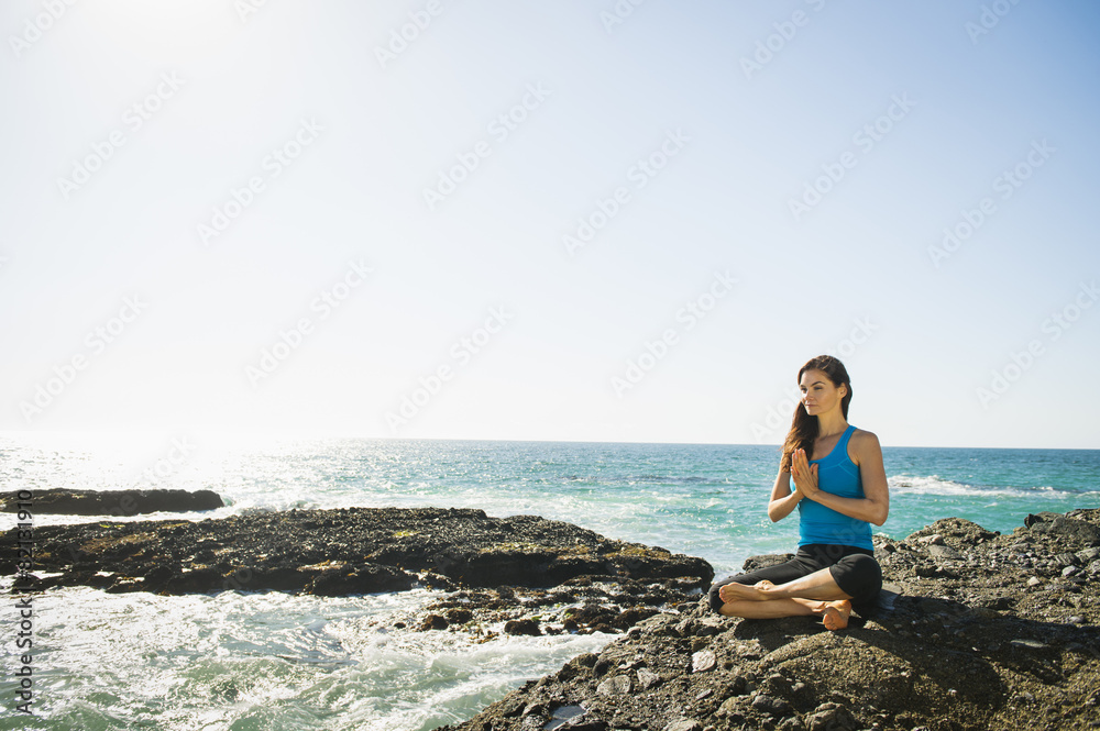 Mixed race woman meditating on rocky beach Mixed race woman meditating on rocky beach
