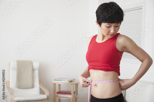 Woman measuring her waist in living room photo