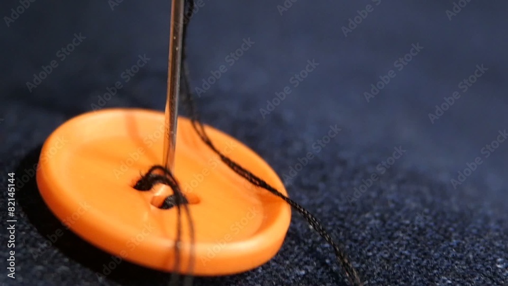 Sewing an orange button on jeans, denim, close up, slow motion Sewing an orange button on jeans, denim, close up, slow motion
