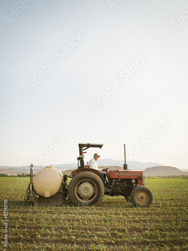 Caucasian farmer driving tractor in crop field