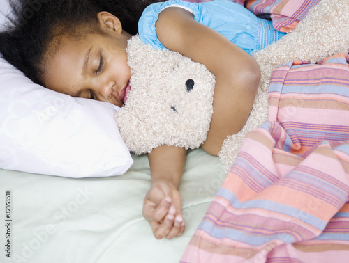 Mixed race girl sleeping with teddy bear