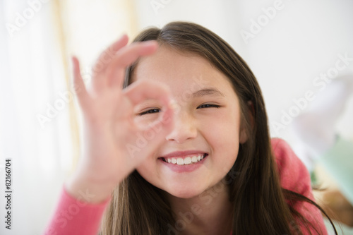Mixed race girl making O.K. sign with fingers