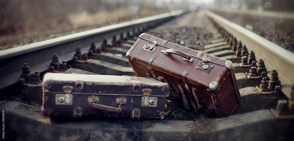 Two vintage suitcases lie on railway rails.