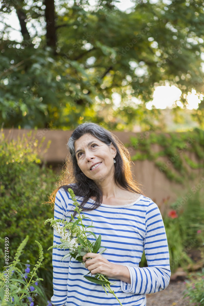 Hispanic woman holding flowers in garden Hispanic woman holding flowers in garden