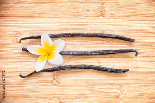 Three vanilla pods with a flower aligned on wooden background