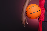 Detail of a basketball player holding a ball against dark backgr