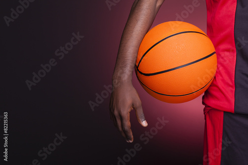 Detail of a basketball player holding a ball against dark backgr