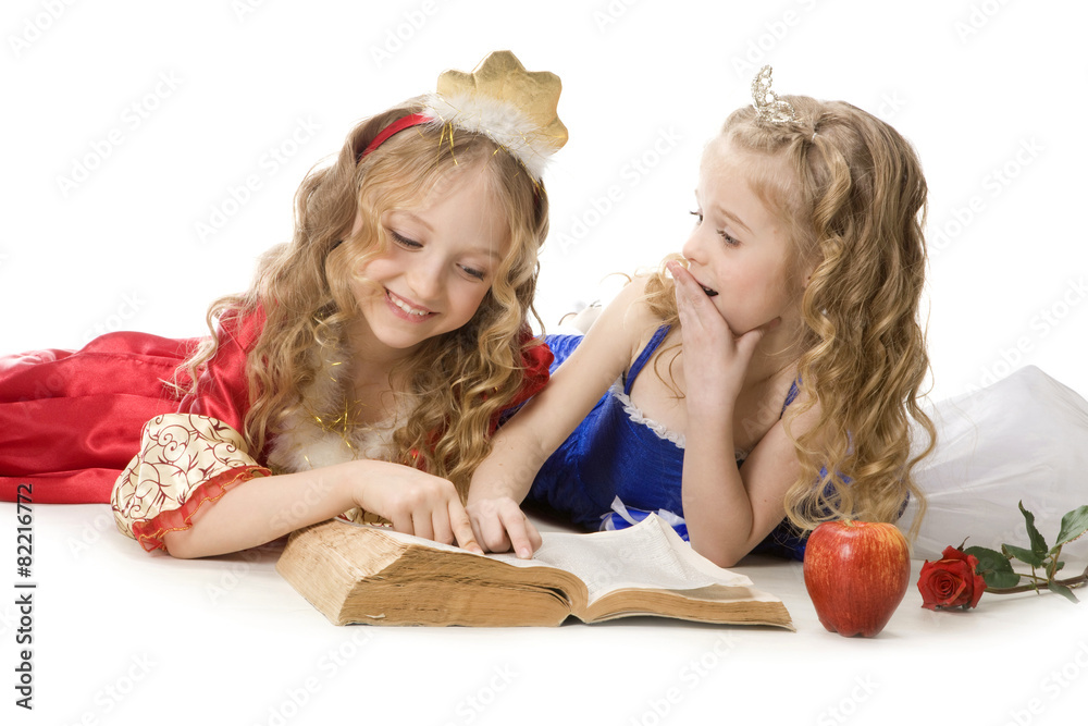 Two beautiful little princesses reading a magic book - obrazy, fototapety, plakaty 