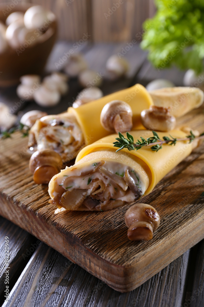 Fototapeta premium Pancakes with creamy mushrooms on cutting board on wooden table, closeup