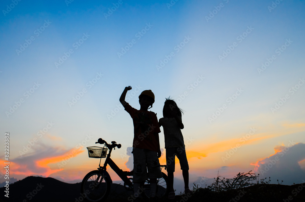 Boy with his sister riding bicycle on sunset background.Silhouet