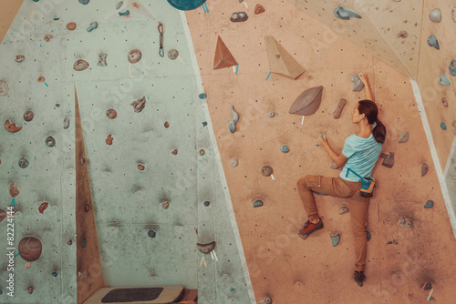 Young woman climbing artificial boulder in gym