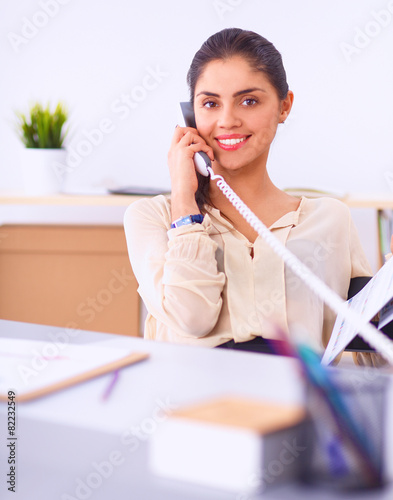 Young businesswoman sitting at the desk and talking on phone