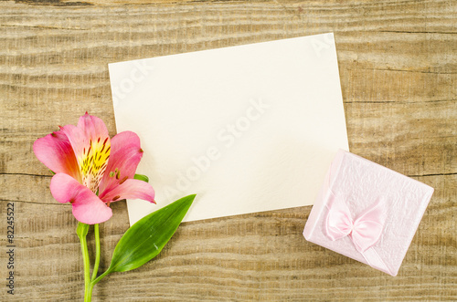Empty card with gift box and flower on wooden background