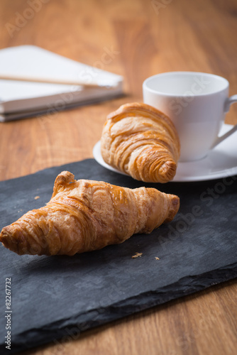 Two tasty french croissants with a cup of coffee and notebook