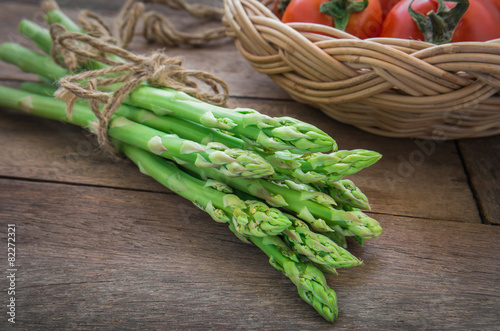 Bunch of asparagus on wooden table and tomato in basket
