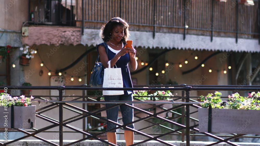 woman walking across a European bridge taking a picture with her cell phone woman walking across a European bridge taking a picture with her cell phone