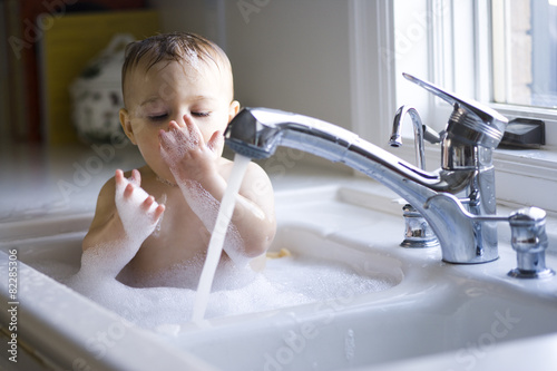 Boy taking bath in kitchen sink