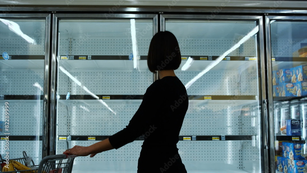 Woman walks by empty freezers at grocery store