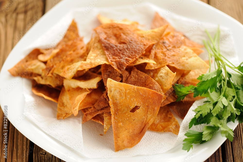 Fried triangle lavash chips in white plate with fresh parsley