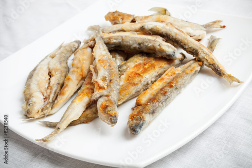 Pile of fried smelts fish lays on a white plate, closeup photo w