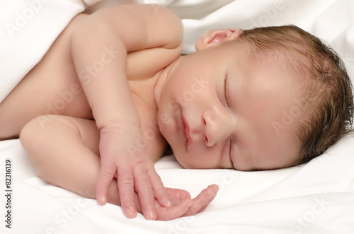 Beautiful innocent newborn sleeping after bath in white sheets