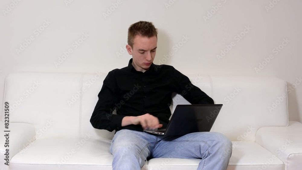 young handsome man sitting on sofa and working on computer young handsome man sitting on sofa and working on computer