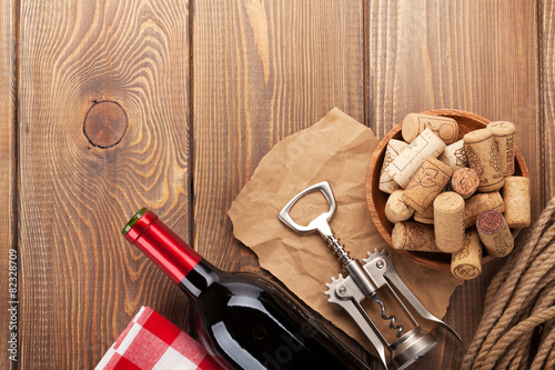 Red wine bottle, corks and corkscrew over wooden table backgroun