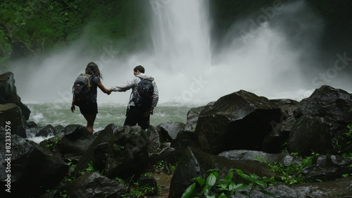 Slow motion wide panning shot of hiking couple admiring waterfall in rain forest / Arenal, La Fortuna, Costa Rica photo