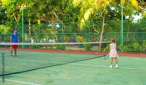 Little girl playing tennis with her dad on the court