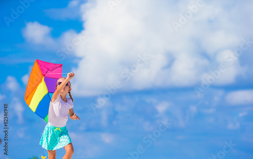 Little happy girl playing with flying kite on tropical beach