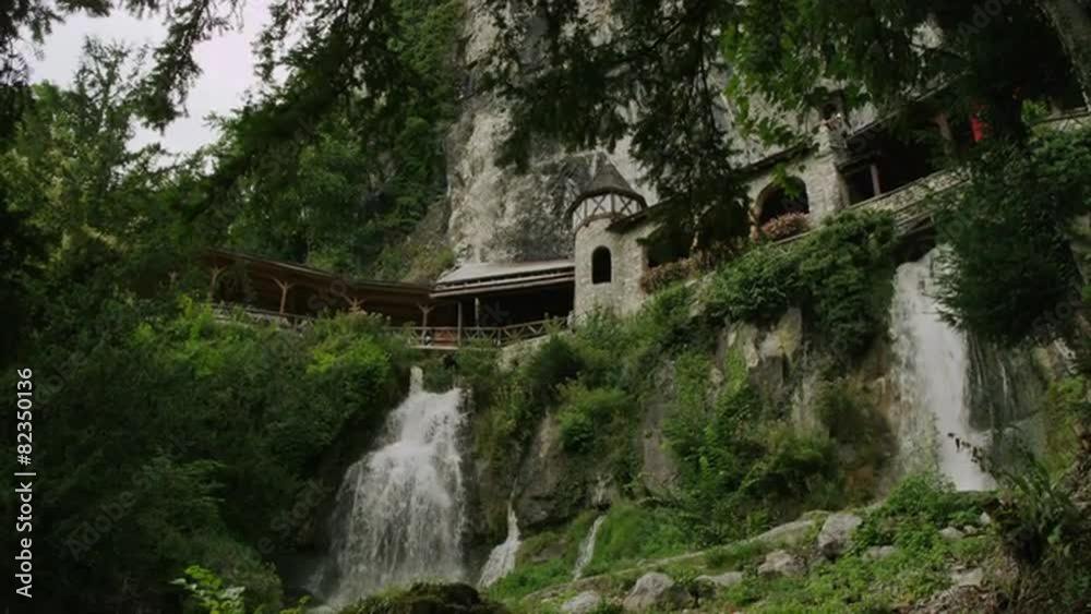Slow motion/medium shot of waterfall and buildings on cliffs / St. Beatus Caves, Switzerland