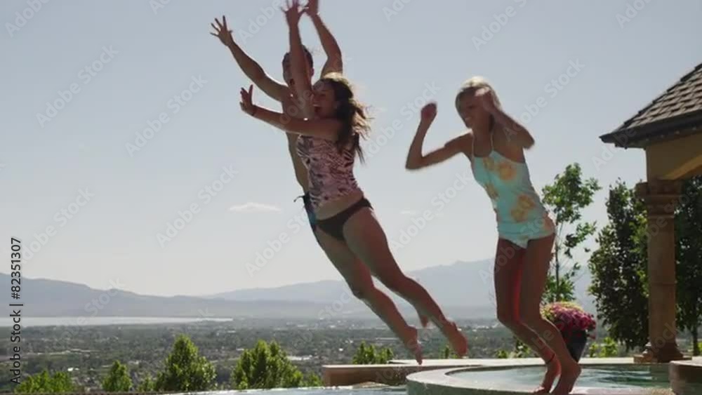 Slow motion, medium shot of girls jumping into swimming pool / Cedar Hills, Utah, United States