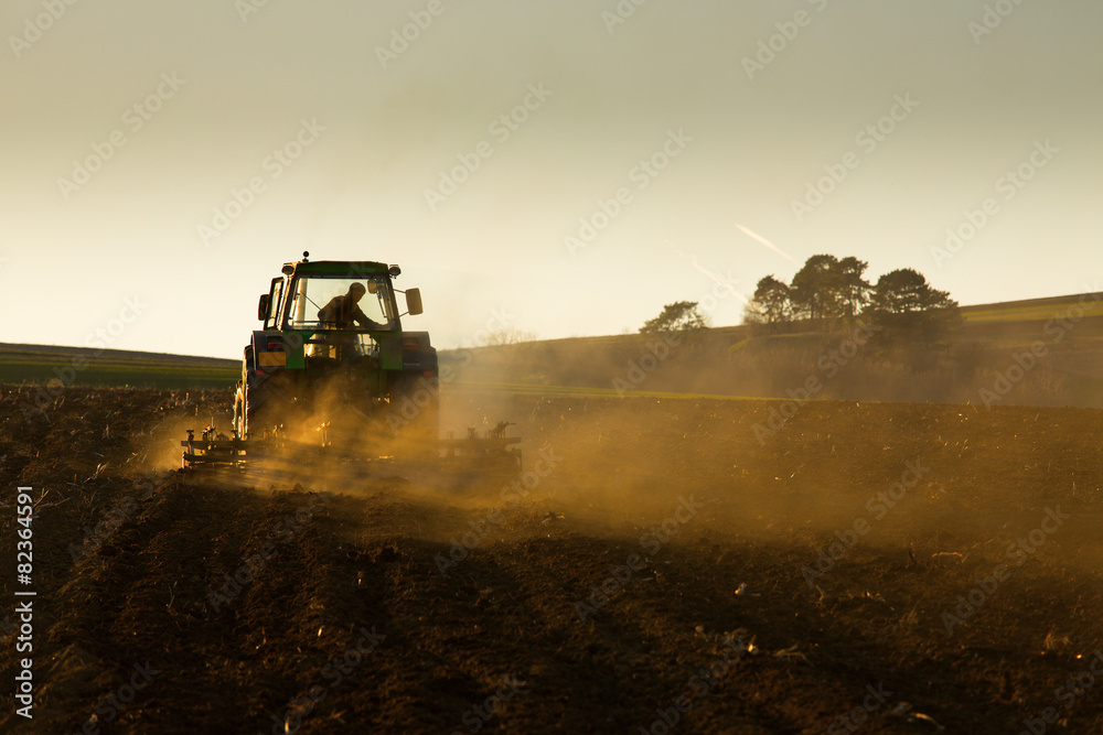 Fototapeta premium Tractor in sunset plowing the field