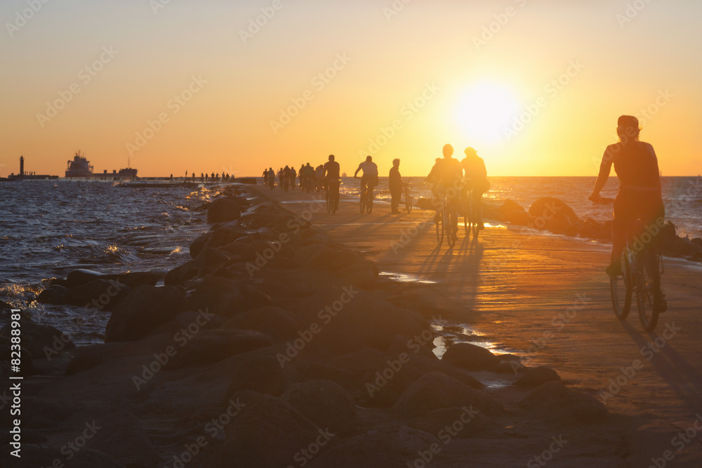 Fototapeta premium People on bikes ride along the dike in the sea at sunset