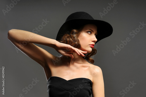Portrait of beautiful model in black dress and hat on gray background