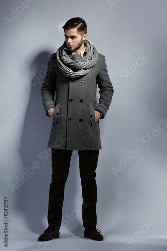 Young man in coat on gray background