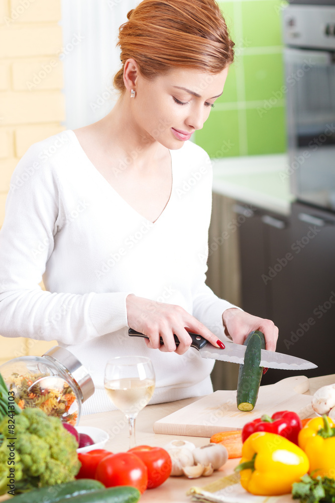 Smiling young woman cutting vegetables in kitchen.