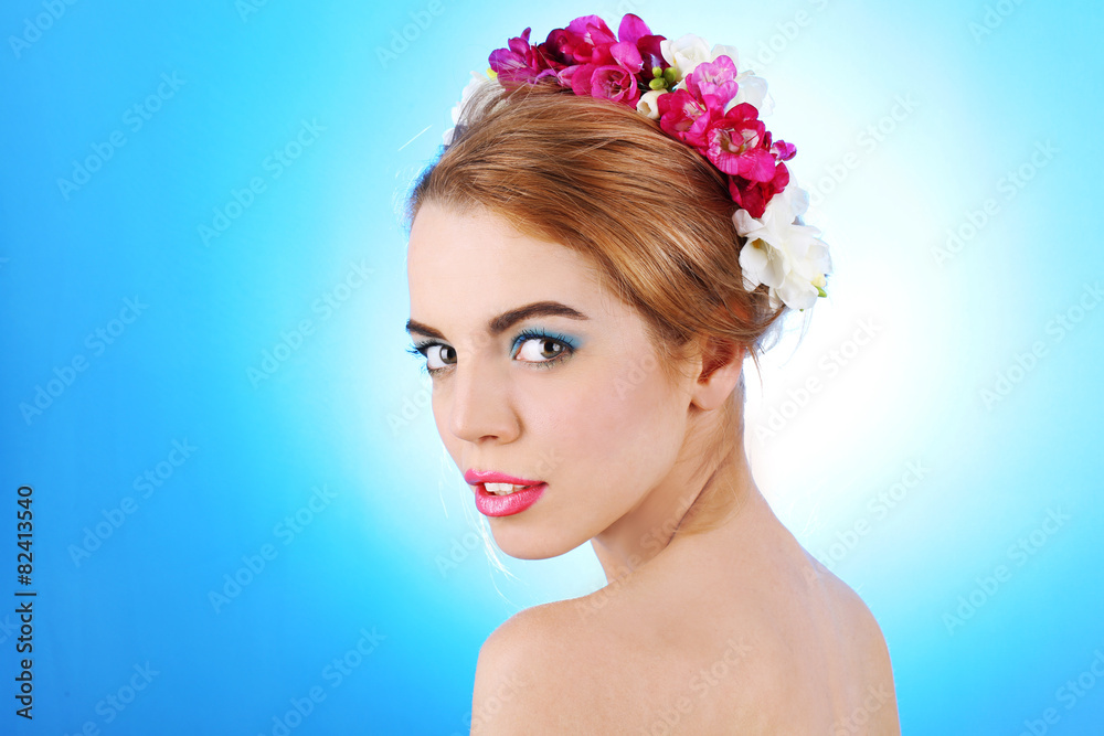Portrait of young woman with flowers in hair on blue background