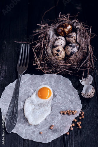 Quail eggs in the nest and a fried egg on a wooden board.