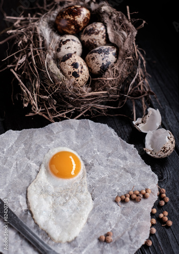 Quail eggs in the nest and a fried egg on a wooden board.
