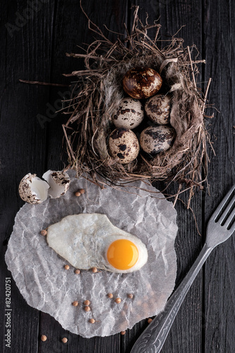 Quail eggs in the nest and a fried egg on a wooden board.