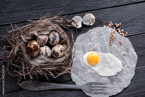 Quail eggs in the nest and a fried egg on a wooden board.