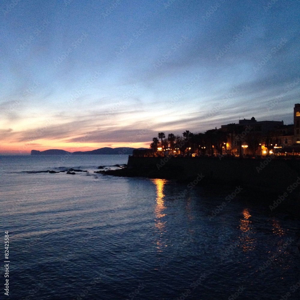 Fototapeta premium sunset and city lights at alghero, sardinia, italy